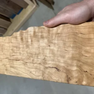 Curly cherry figured board held in hand at G&H Hardwoods, showing tight rippled grain and warm amber color.